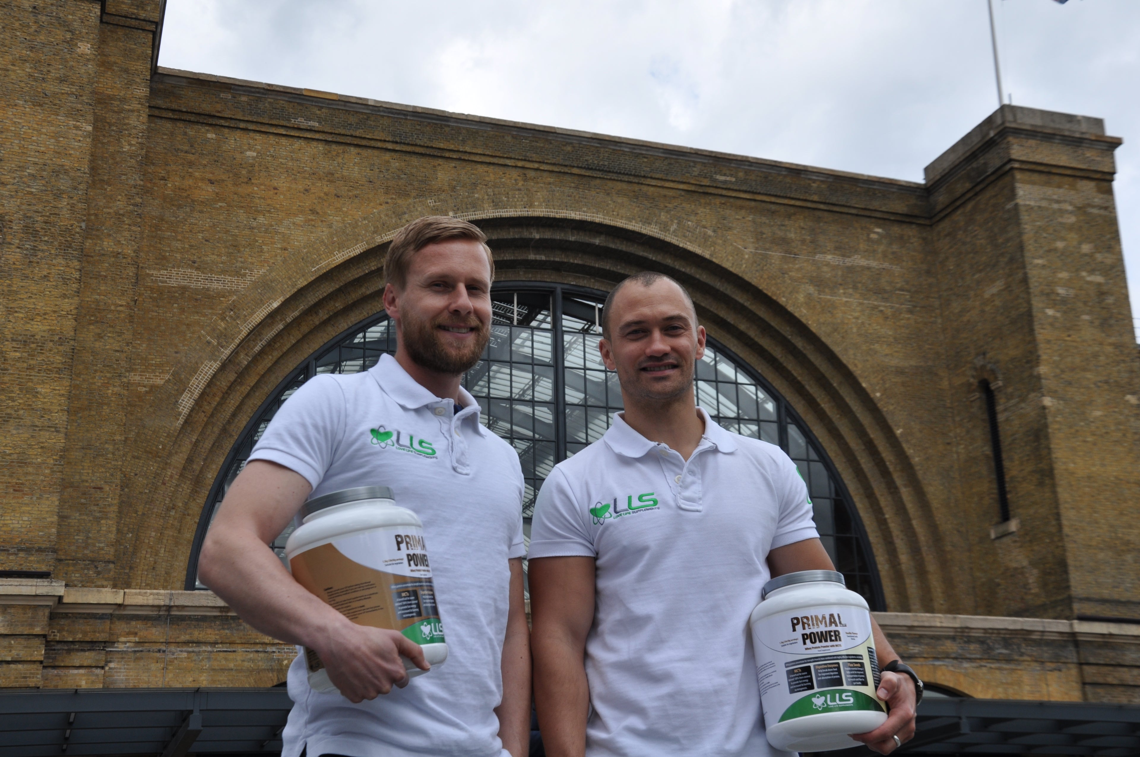 love life supplements Two men in white polos with a brand logo stand in front of a large stone archway.
