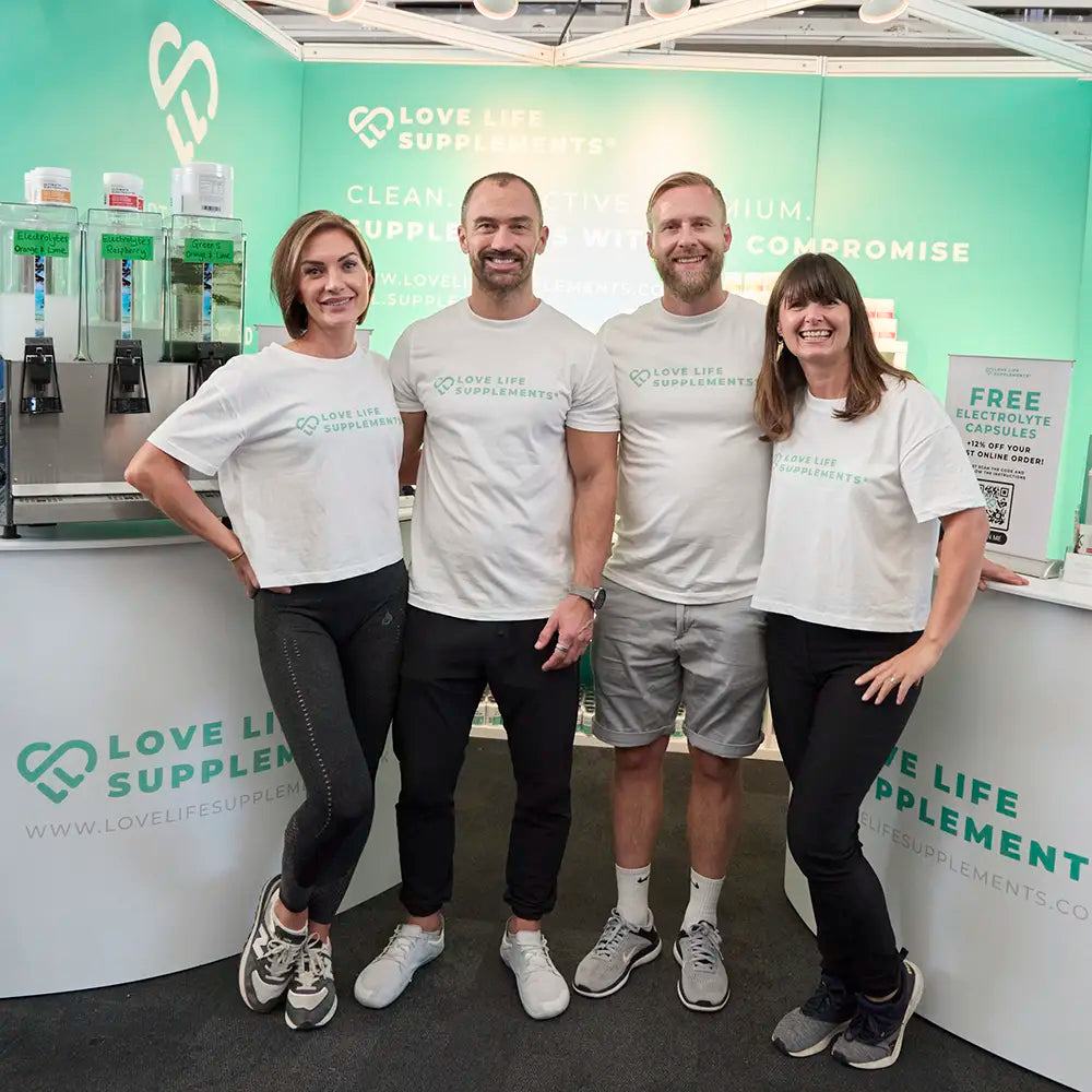 love life supplements team Four people in matching white t-shirts standing in front of a Love Life Supplements booth.