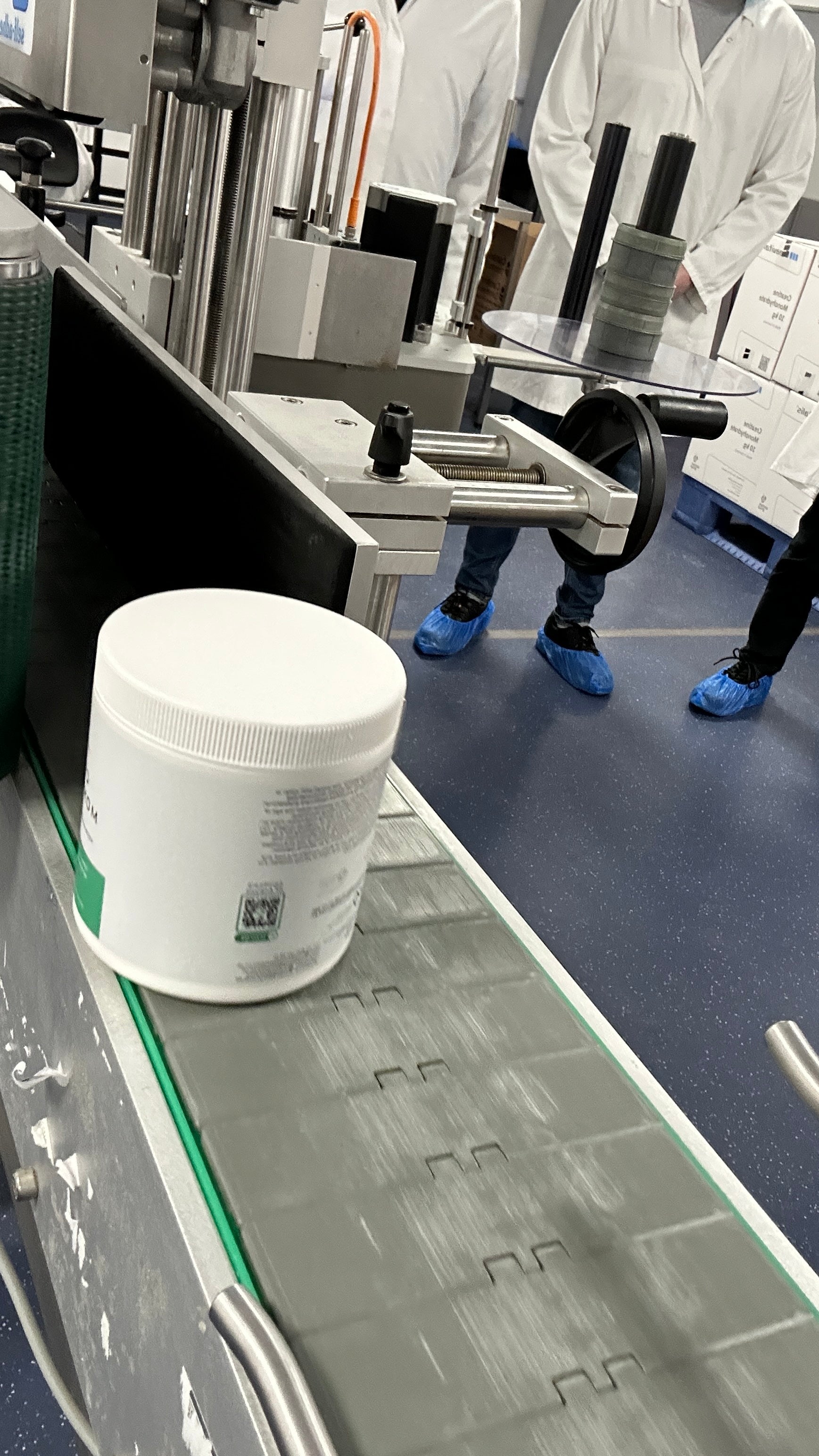 Container on a conveyor belt with people in lab coats in the background